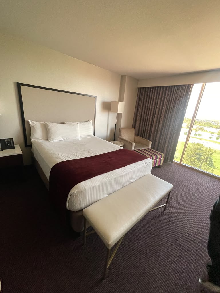 King guest room with upholstered headboard, bench, lounge chair, floor lamp and window wall