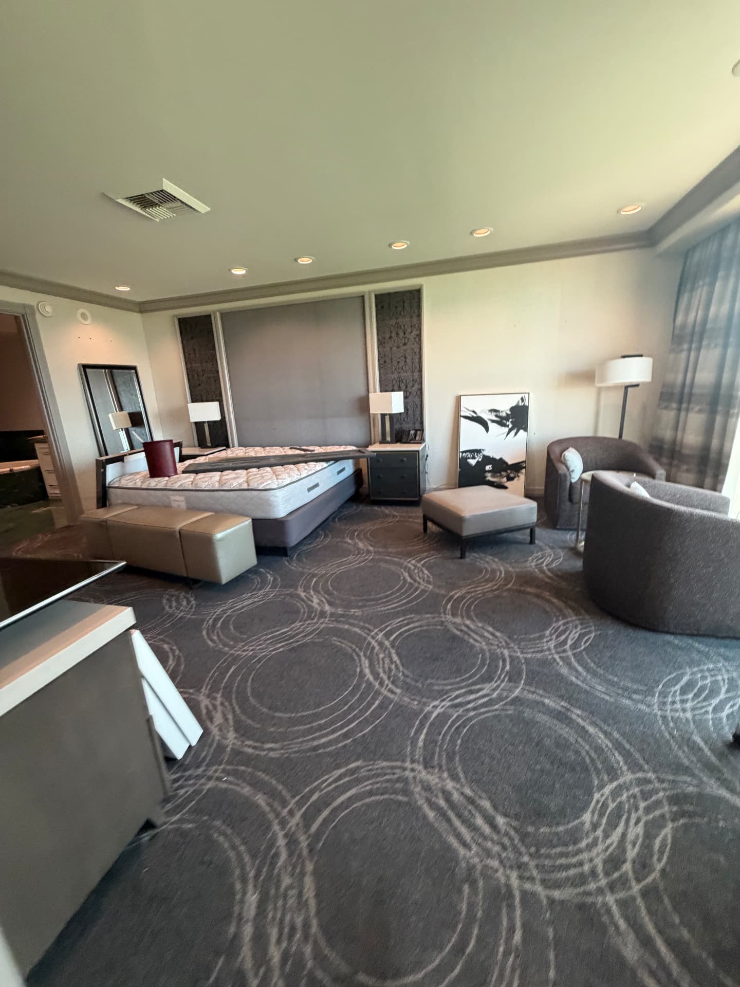 Wide view of a suite bedroom with king bed, nightstands, lamps, benches and lounge chairs
