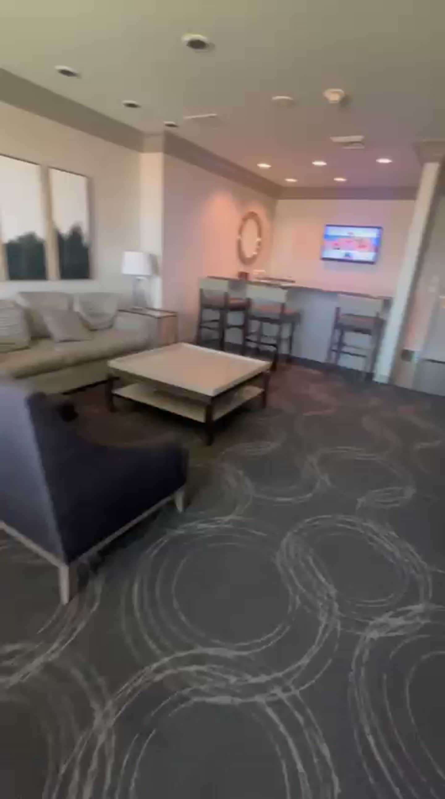 Suite living area with sofa, lounge chair, coffee table, wall art and wet bar with counter stools