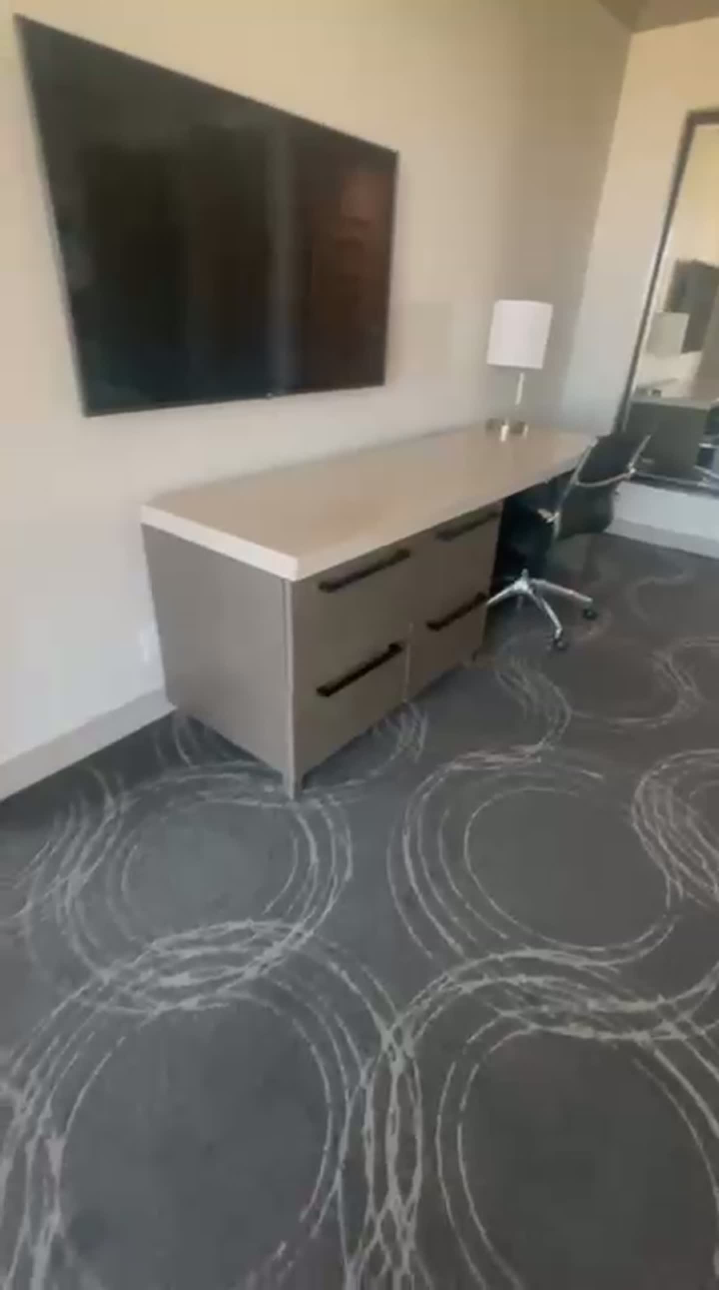 Suite work area with long desk, dresser, task chair, table lamp and large flat-screen TV