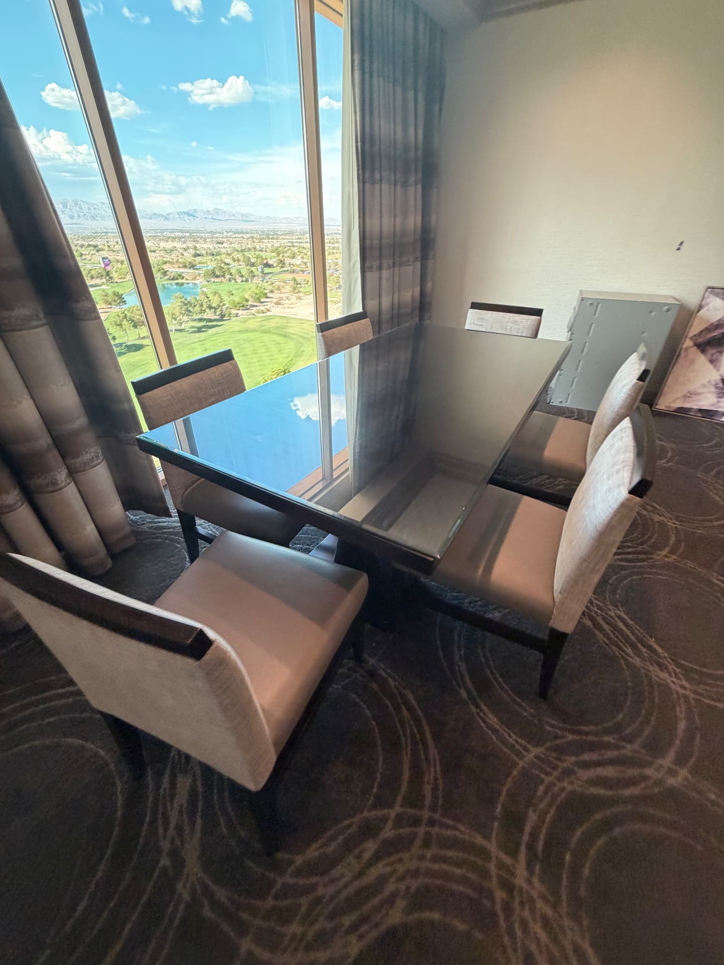 Suite dining table with glass top and four upholstered chairs beside a floor-to-ceiling window