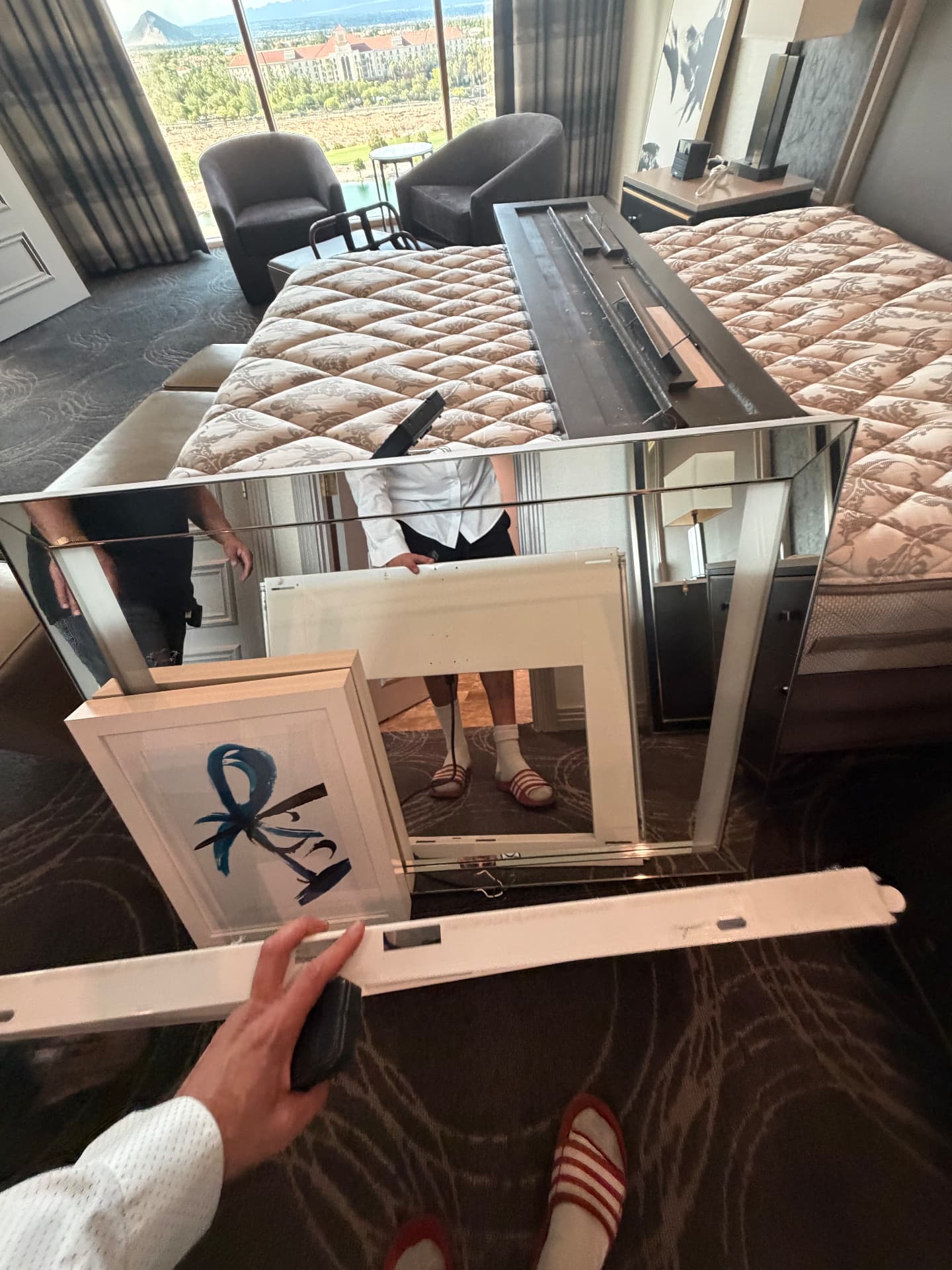 Mirrored console, framed artwork and light fixtures staged beside a king bed in a suite